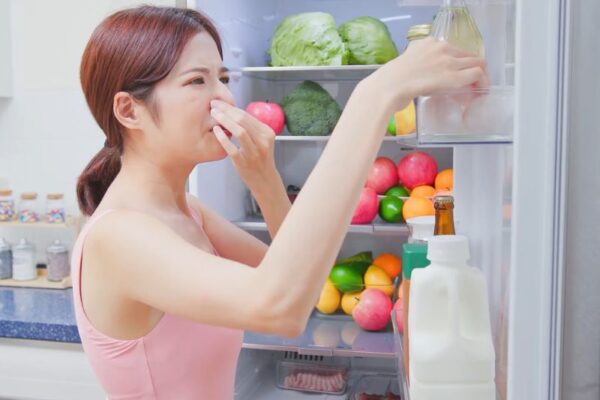 Kako se rešiti neprijatnih mirisa iz frižidera bez hemije devojka se drži za nos pored otvorenog frižidera koji smrdi
