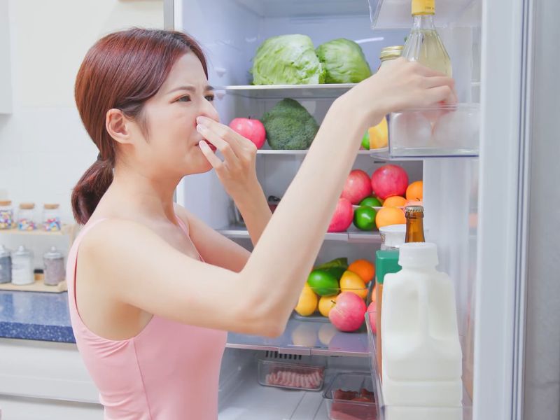 devojka se drži za nos pored otvorenog frižidera koji smrdi