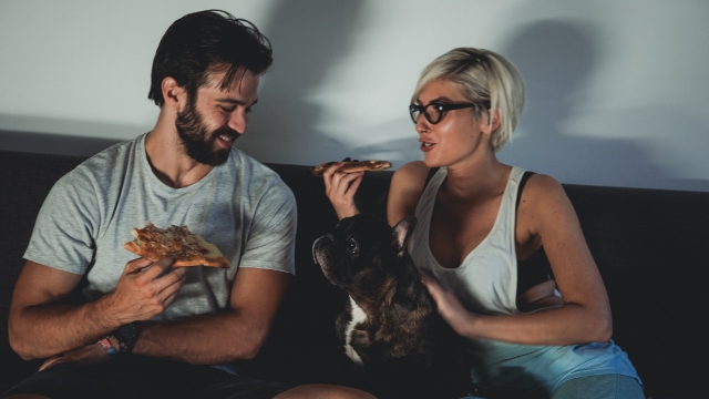 Par sedi na kauču sa psom, dok jedu picu