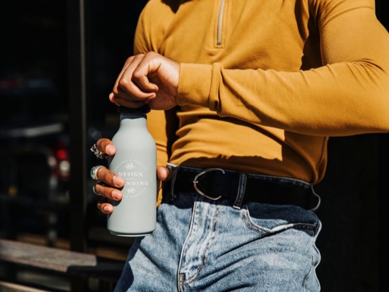 Muškarac u žutoj majici dugih rukava otvara sivu bocu sa vodom