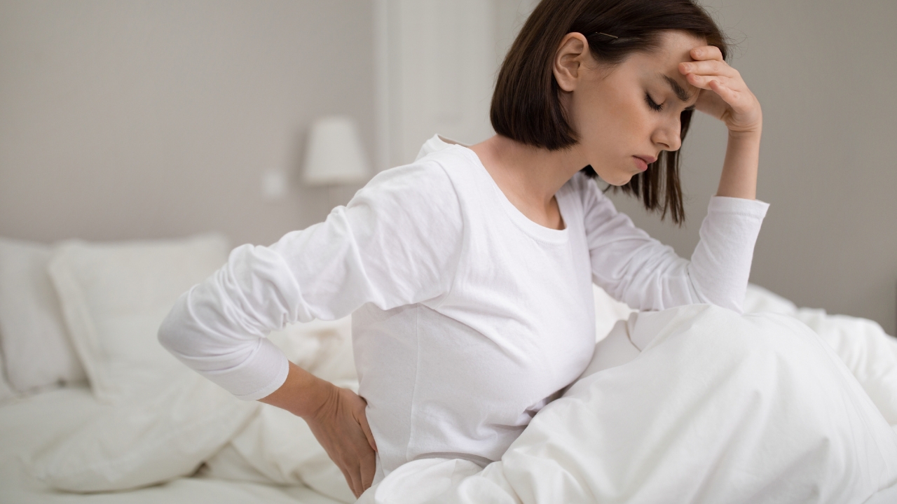 Žena sedi u krevetu i drži se za donji deo leđa zbog bola nakon buđenja