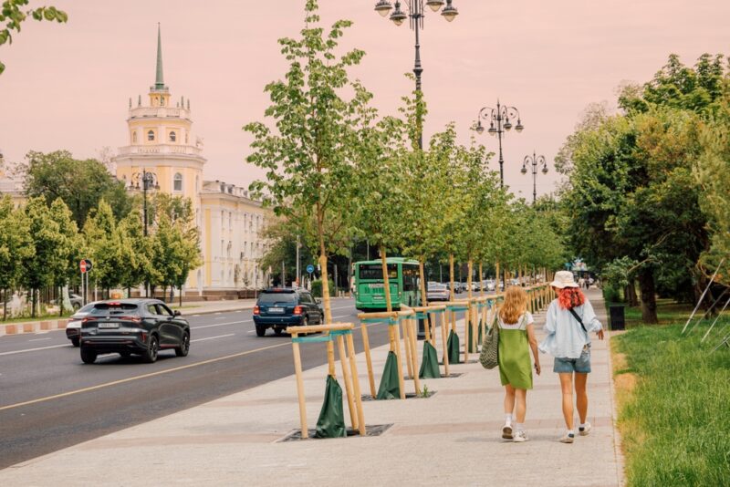 Gradska ulica sa saobraćajem gde električni i hibridni automobili prolaze pored pešaka i drvoreda