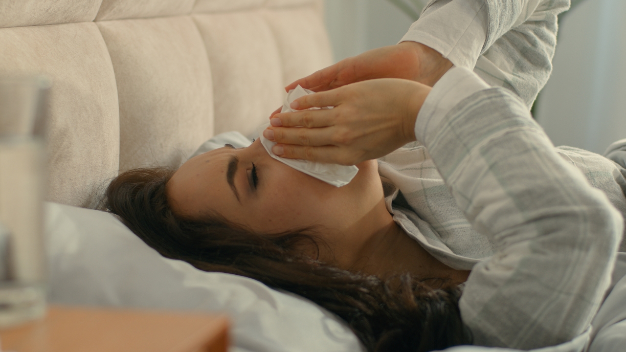 Žena leži u krevetu i briše nos maramicom zbog kijanja i zapušenosti