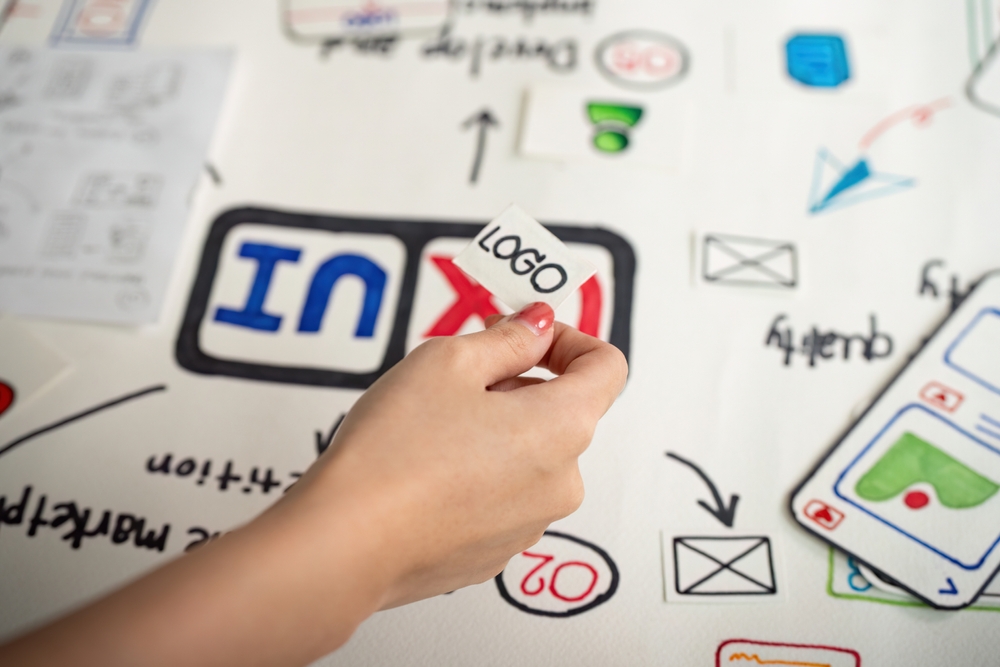 Ruka postavlja element logotipa na skicu brenda, simbolizujući proces osmišljavanja vizuelnog identiteta i razvoja upečatljivog dizajna