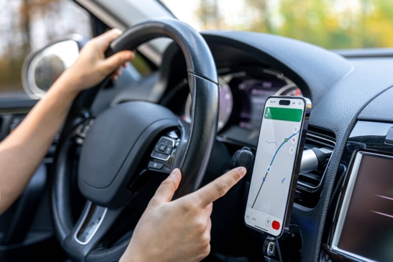 Vozač koristi navigacionu aplikaciju na mobilnom telefonu za pronalaženje punjača za električni automobil tokom putovanja.