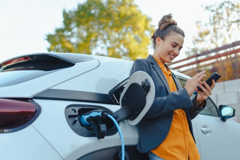 Vozač koristi mobilni telefon dok se električni automobil puni na punjaču pored benzinske stanice u Crnoj Gori